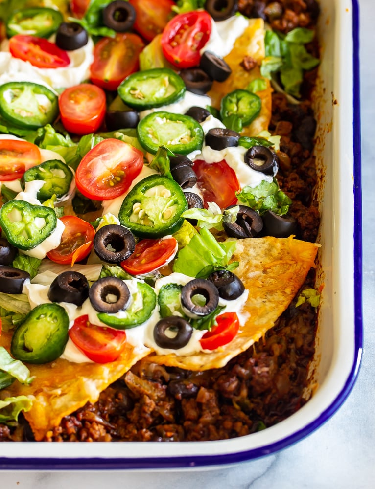 A pan with taco seasoned ground beef topped with shredded cheeses and tortilla chips and jalapenos, beans and tomatoes