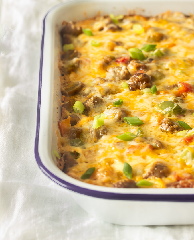 A tater tot breakfast casserole in a pan with crispy tater tots, eggs, melted cheese, sausages, peppers and onions. 