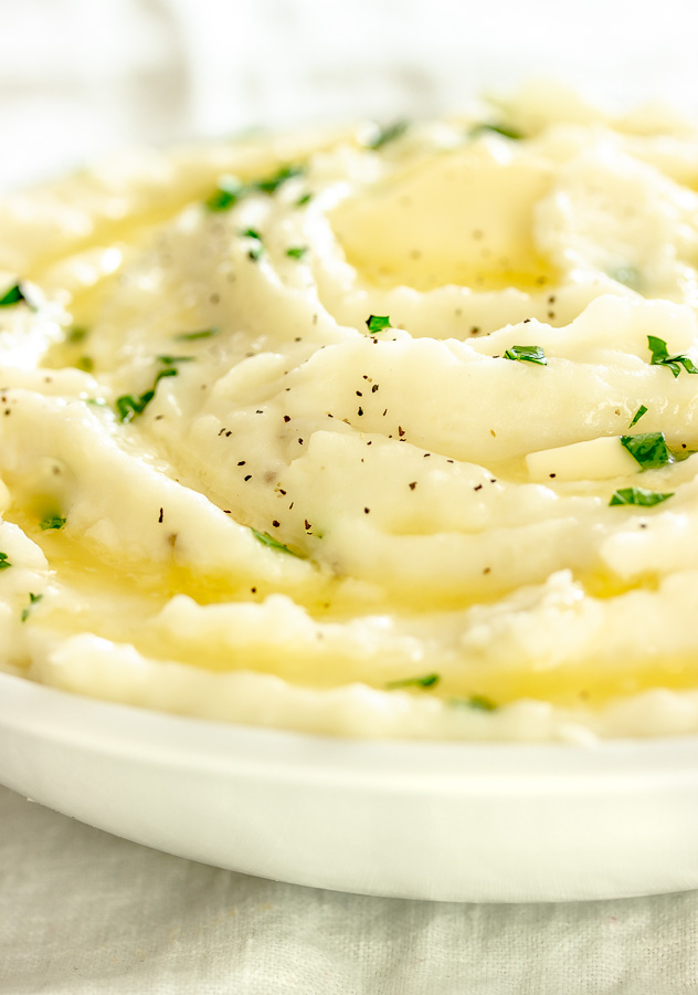 A bowl of creamy mashed potatoes with melted butter and garnished with parsley