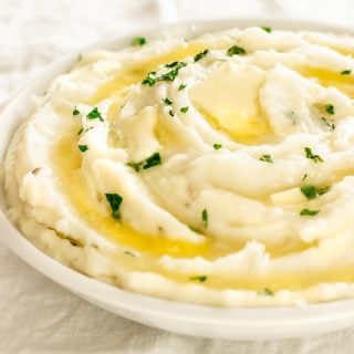 A bowl of creamy mashed potatoes with melted butter and garnished with parsley