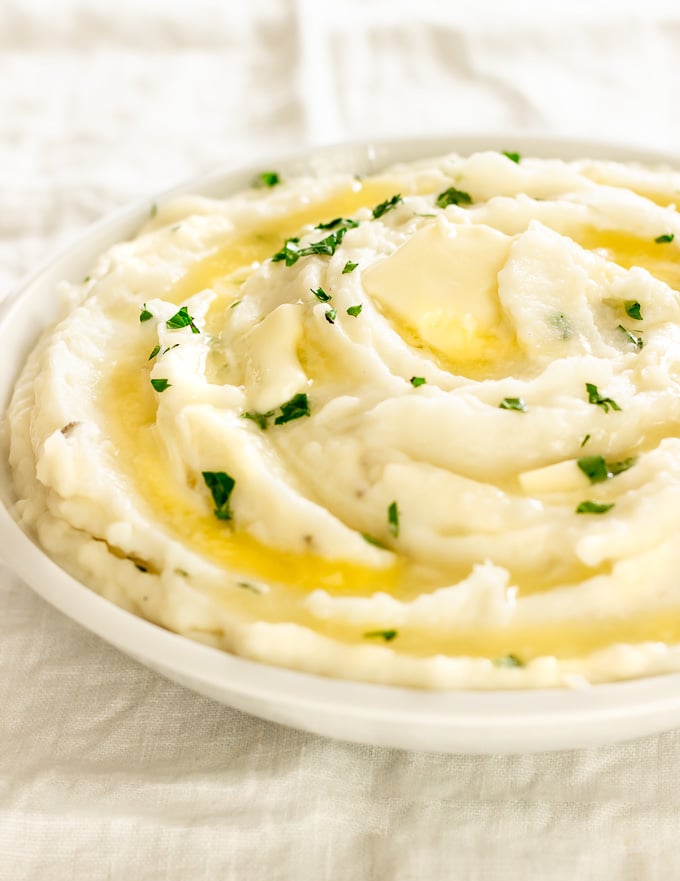 A bowl of creamy mashed potatoes with melted butter and garnished with parsley