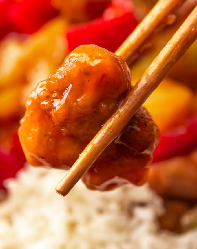 A picture of chopsticks holding a pice of sweet and sour chicken
