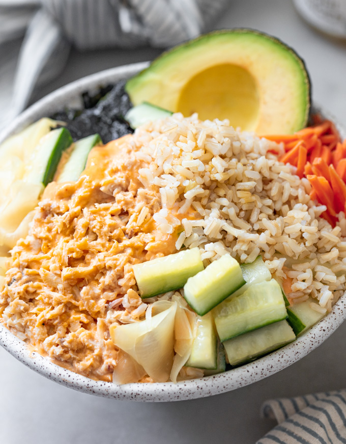 A tuna fish bowl with pickled cucmbers, carrots brown rice topped with spicy mayonnaise