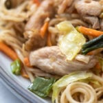 A plate of chicken chow mein with cabbage, green onions, carrots and bean sprouts