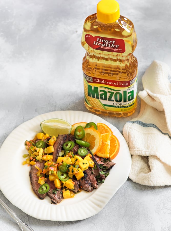 Jerk steak with mango salsa on a white plate with a bottle of mazola heart healthy corn oil behind it