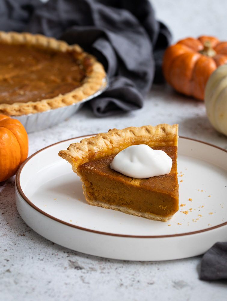 A photo of condensed milk pumpkin pie on a white plate topped with whipped cream