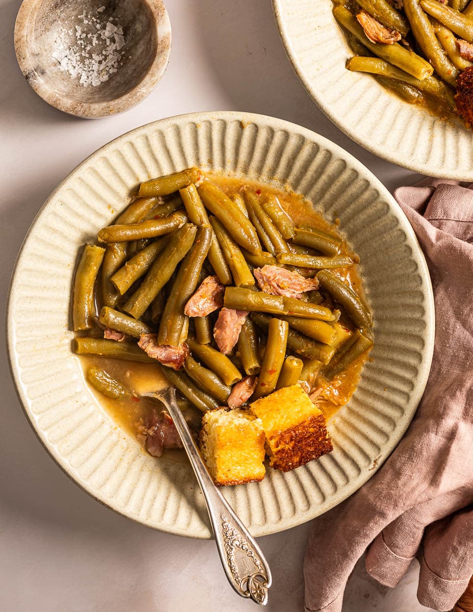 A picture of two bowl of southern soul food green beans with smoked turkey and side of cornbread.