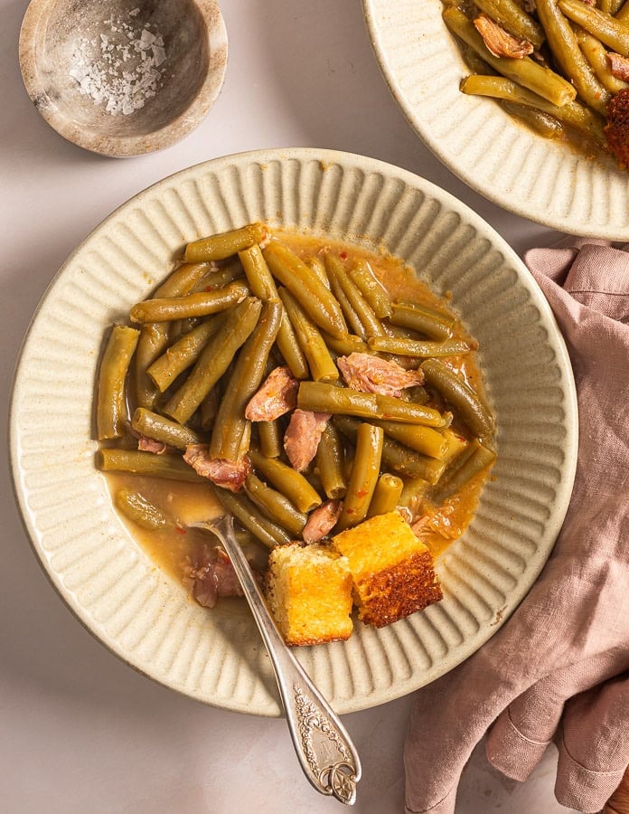 A picture of two bowl of green beans with smoked turkey and side of cornbread.