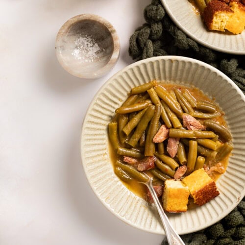 A picture of two bowl of soul food green beans with smoked turkey and side of cornbread.