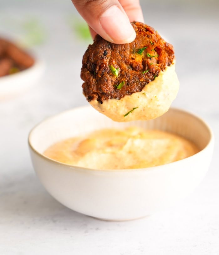 A crispy black-eyed pea patty being dipped into a small bowl of Cajun sauce, showcasing its golden, crunchy texture.