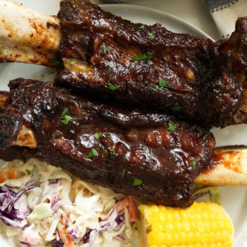 A picture of oven baked beef ribs with bbq sauce on a plate with southern coleslaw and buttered corn.