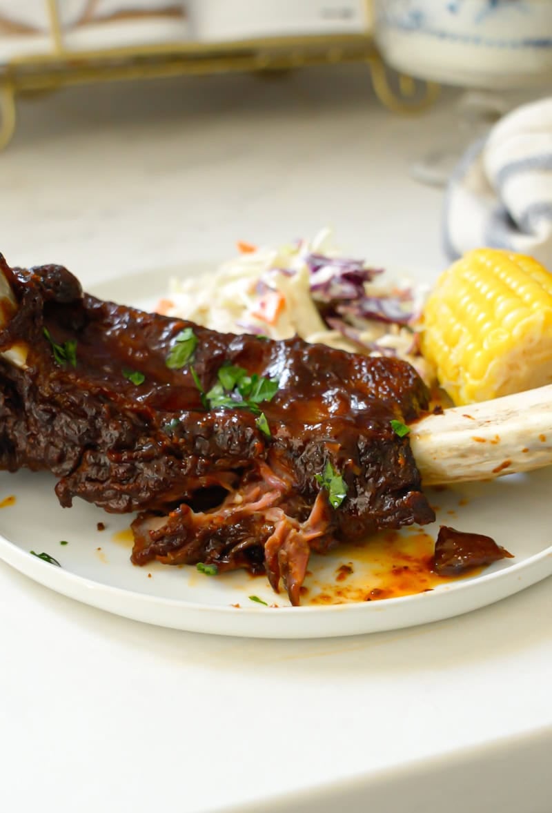 easy beef ribs with bbq sauce on a plate with coleslaw and corn