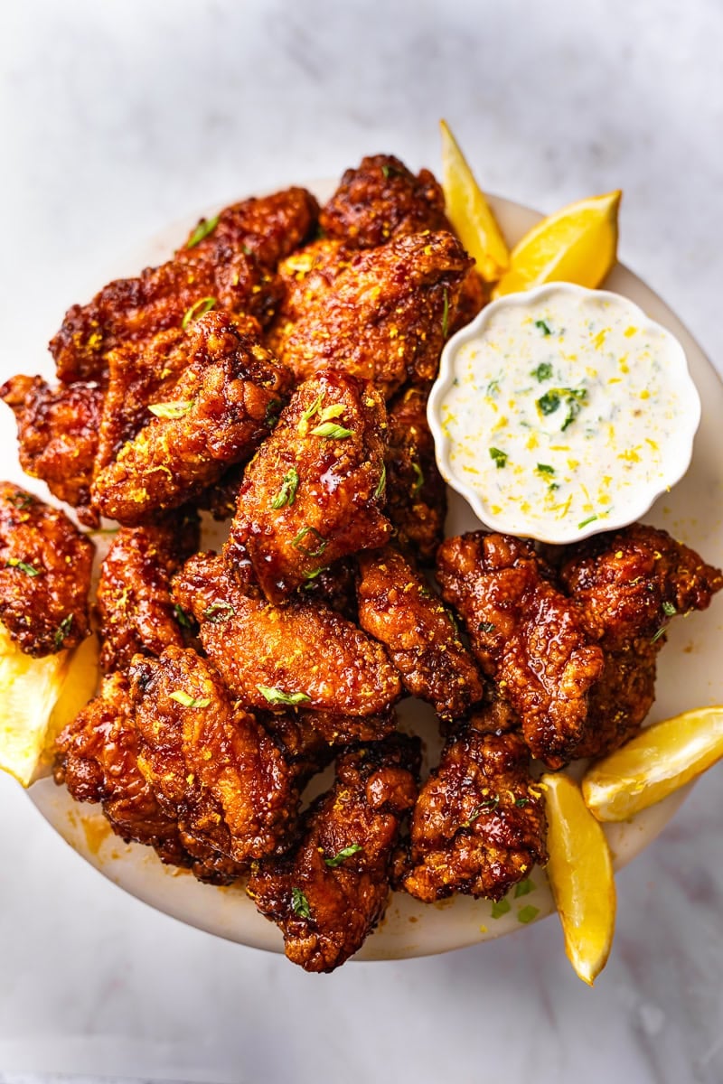 A plate of garlic soy chicken wings, garnished with green onions and lemon sauce with a side of ranch dressing. 