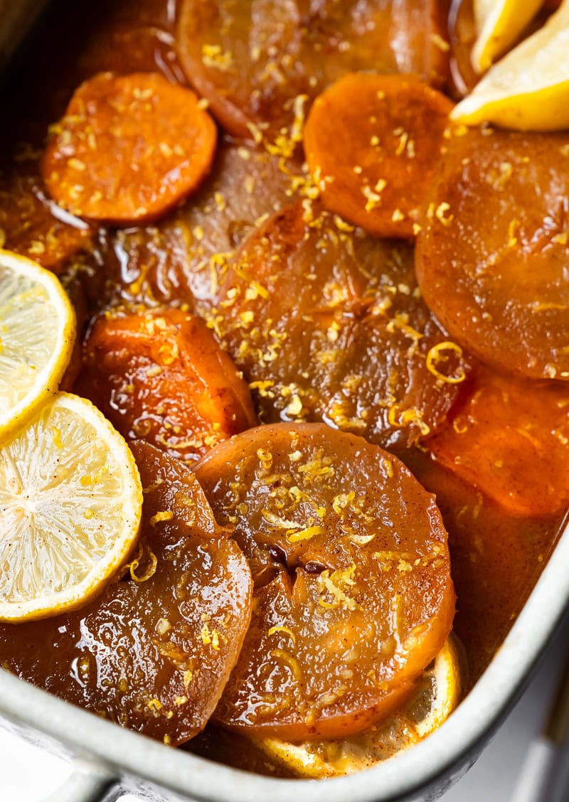 Close-up of baked slices of sweet potato apple casserole with caramel glaze and citrus garnish.