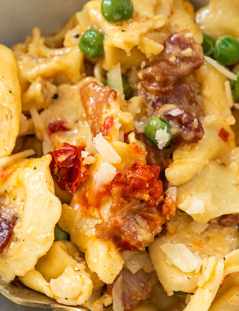 A closeup of cheese tortellini carbonara with bacon in glossy cream sauce
