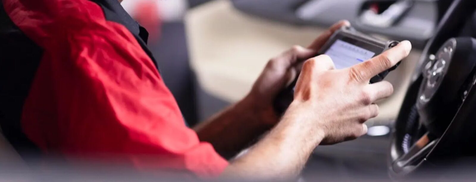 Auto repair technician using a smartphone inside a vehicle.