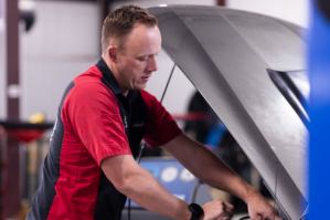Auto repair technician checking under the hood of a vehicle for maintenance.