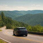 Black SUV driving on a winding mountain road with lush green trees and hills.