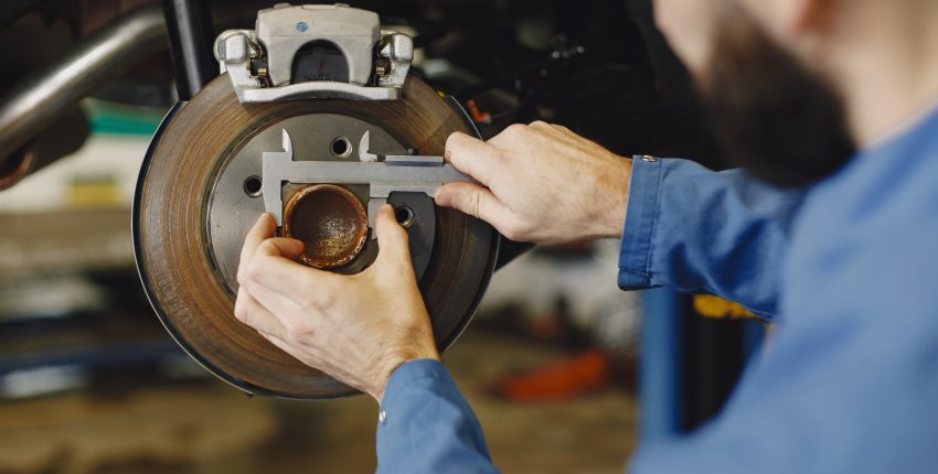 Technician inspecting a brake disc with a wrench and ratchet in an auto repair shop.