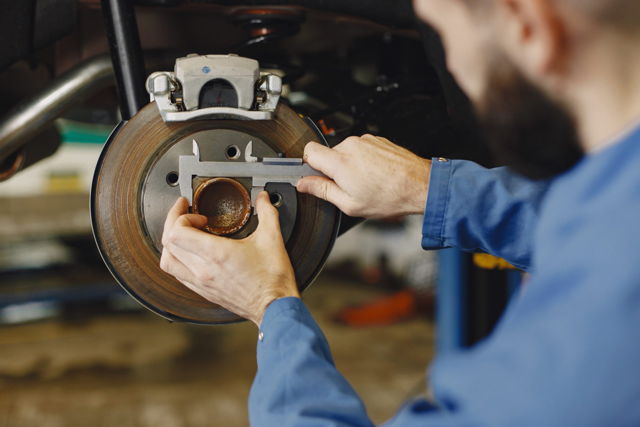 Technician inspecting a brake disc with a wrench and ratchet in an auto repair shop.