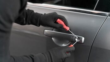 Technician repairing car door lock with screwdriver, focusing on vehicle maintenance.