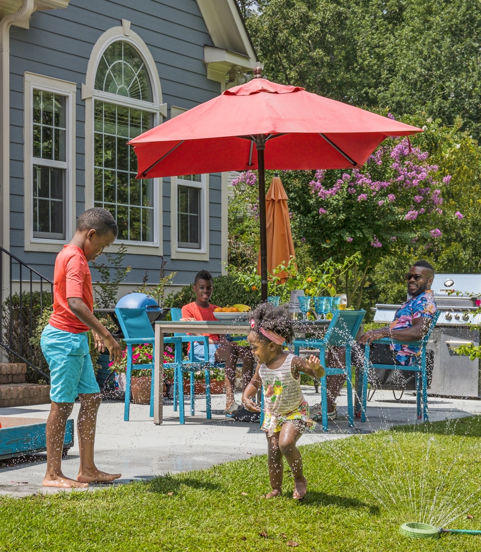 kids playing in sprinkler in yard next to patio