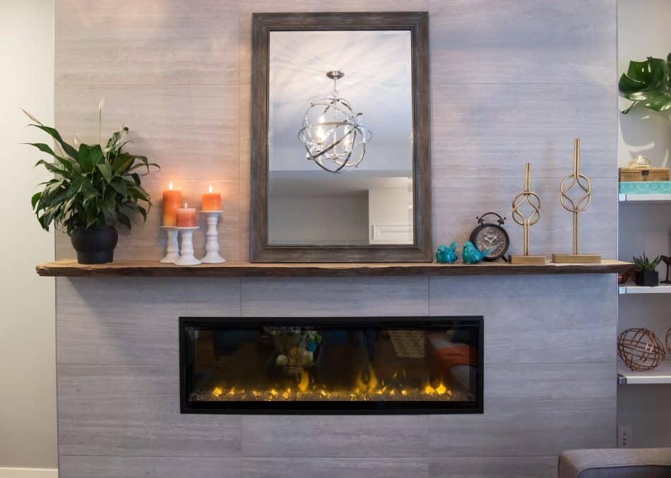 Modern fireplace with a wooden mantel, mirror, candles, plant, gold sculptures, and decorative accents