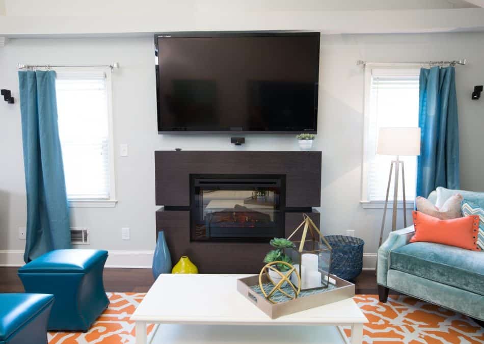 Colorful living room with wall-mounted TV, fireplace, blue curtains, and vibrant decor
