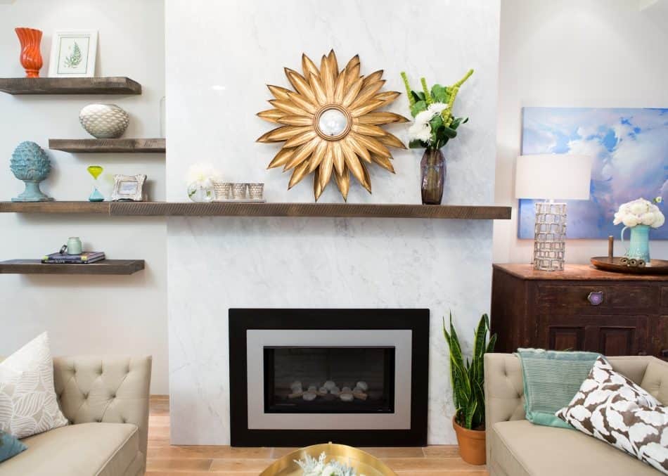 Elegant living room with marble fireplace, gold sunburst mirror, floating shelves, and colorful decor