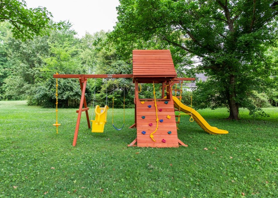 Wooden backyard playset with swings, slide, climbing wall, and rope ladder