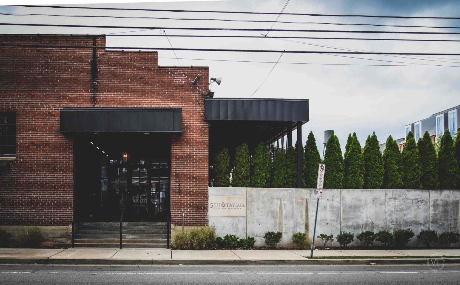 Brick building with black awnings, concrete wall, and greenery