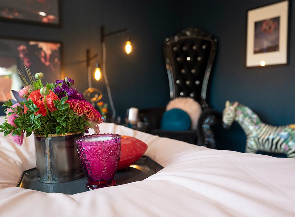 Moody bedroom with dark walls, tufted chair, zebra statue, and tray with flowers and candle