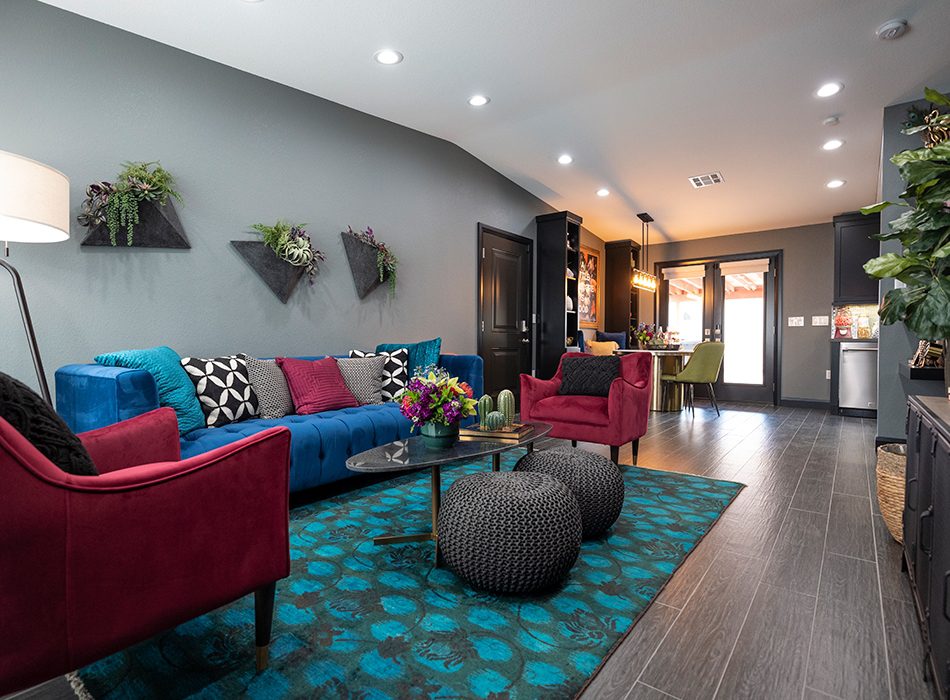 Colorful living room with blue sofa, red chairs, patterned rug, and wall-mounted planters