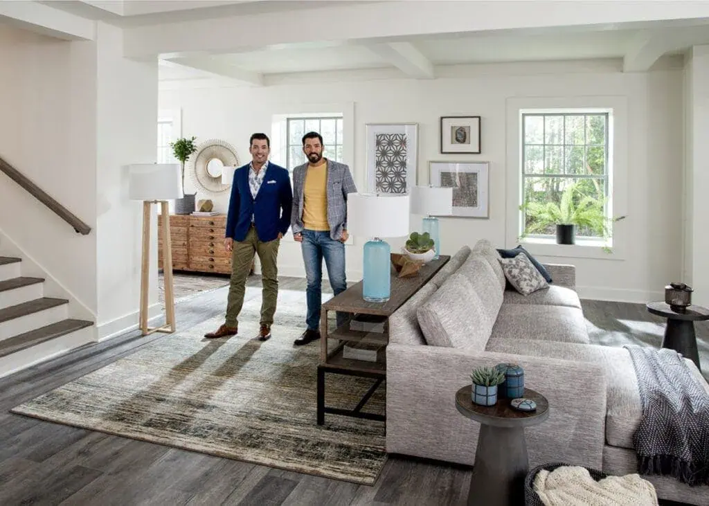 Drew and Jonathan Scott standing in a bright, modern living room with neutral decor.