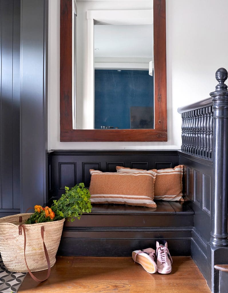 Cozy entry nook with black bench seating, striped pillows, a large mirror, and a tote bag