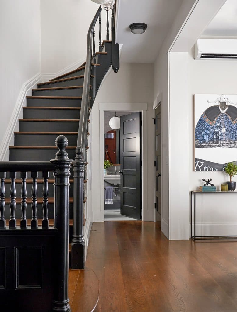 Stylish hallway with curved black staircase, wood flooring, and open door to a bathroom
