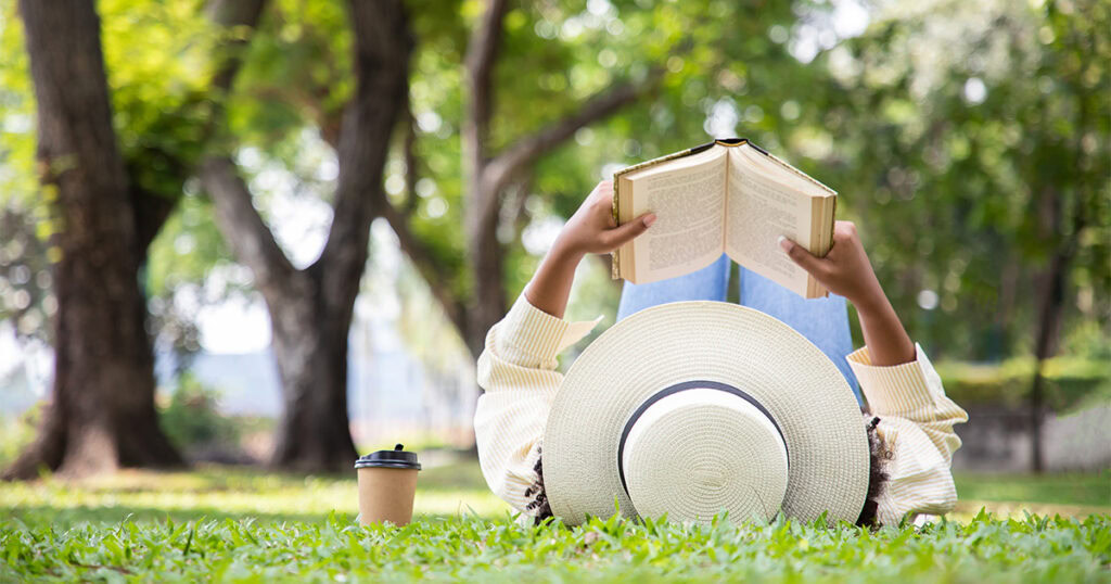 Person lying on grass in a park, reading a book with a sunhat on