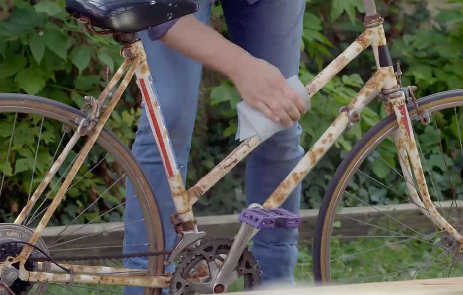 Person cleaning a rusty bicycle frame outdoors