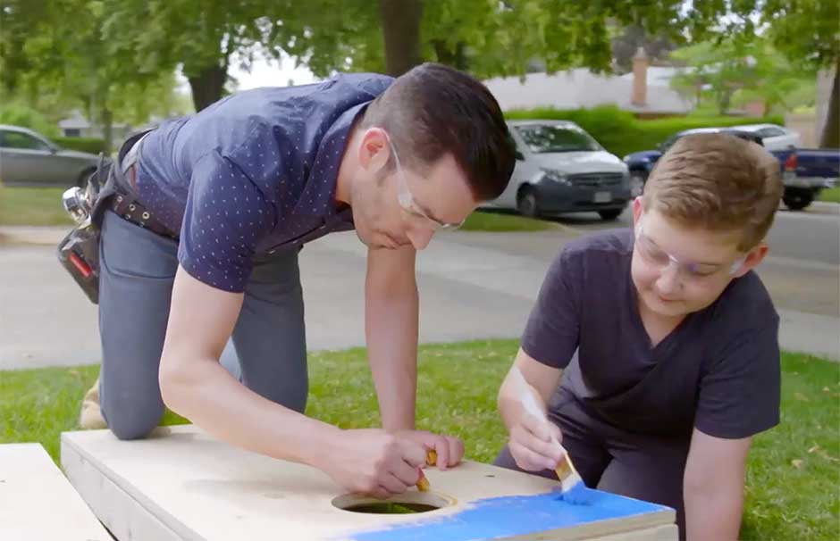 Jonathan Scott and boy painting a wooden board outdoors