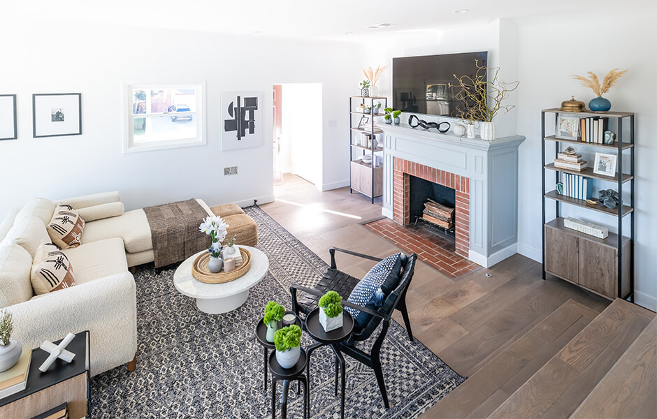 Bright living room with a sectional sofa, brick fireplace, open shelving, and patterned rug