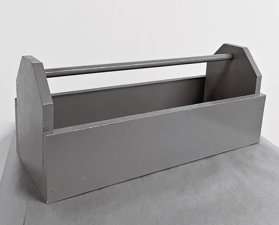 Simple gray wooden toolbox with a handlebar, placed on a gray surface against a white background