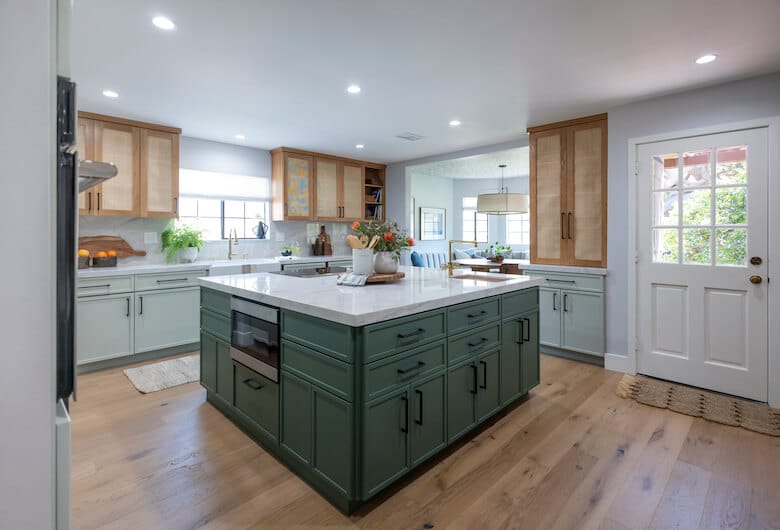 Bright kitchen with a green island, wood flooring, light wood upper cabinets, and white countertops