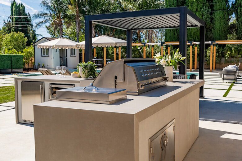 Outdoor kitchen with built-in grill, modern cabinetry, and a shaded pergola