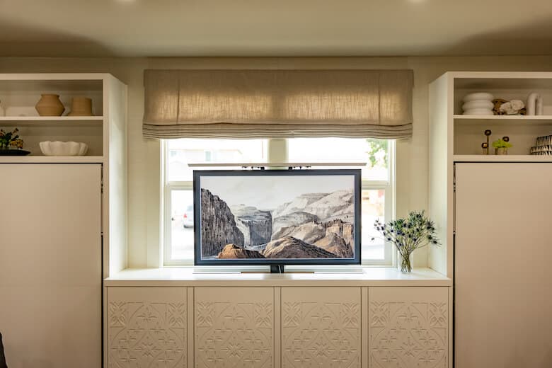 Window with Roman shade, TV, and built-in white cabinets