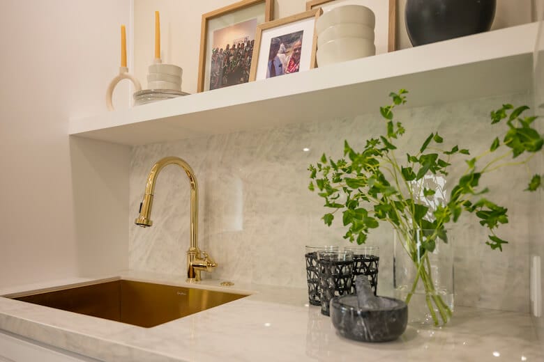 Marble countertop with gold faucet, green vase, and decor