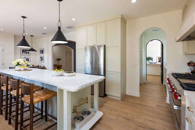 Kitchen with white island, wooden stools, black pendant lights, and stainless steel appliances