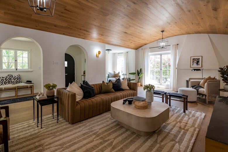 Spacious living room with a brown sofa, light wood ceiling, large windows, and neutral-toned decor