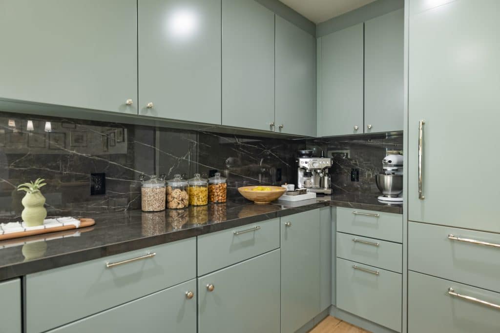 Kitchen corner with light green cabinets, dark marble countertop and backsplash, and small appliances