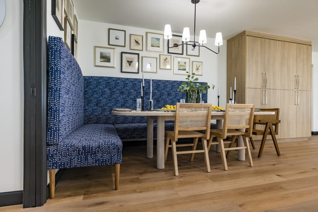 Dining nook with blue patterned bench, wooden chairs, framed photos, and wood flooring