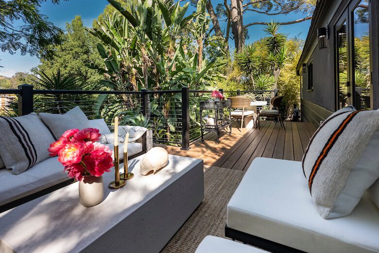 Outdoor patio with white cushioned seating, tropical plants, and a wooden deck
